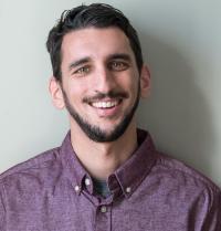 A smiling bearded man in a purple button-down shirt